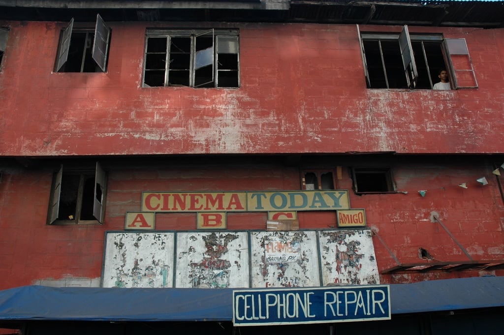 Red cinema building with windows and a sign cellphone repair.