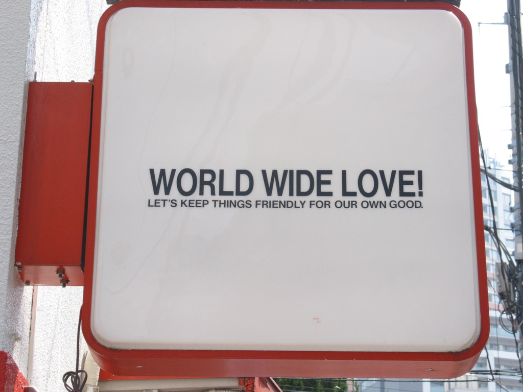 a street sign with the following words: World Wide Love. LET'S KEEP THINGS FRIENDLY FOR OUR OWN GOOD.